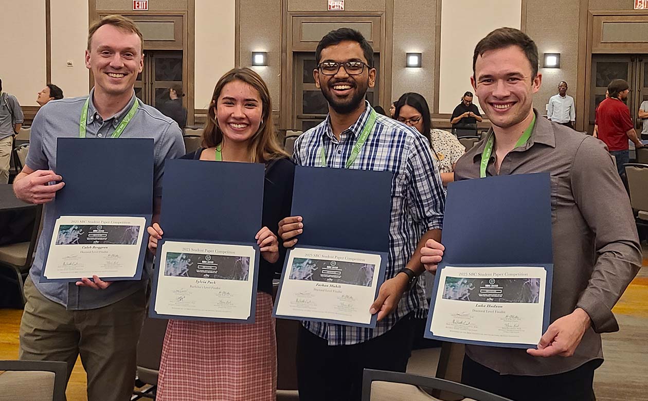 Four people stand with finalist certificates